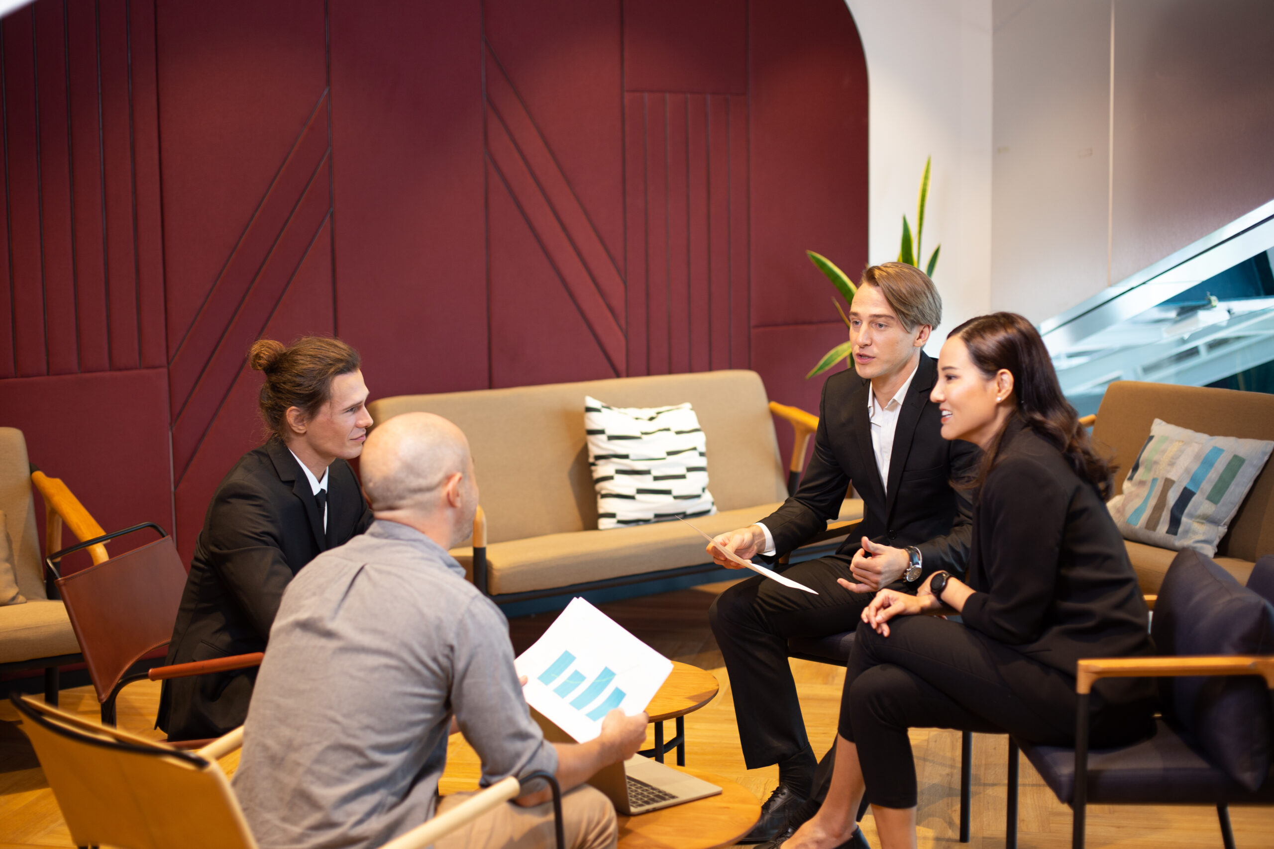 Eine Frau und drei Männer in Businesskleidung besprechen in einer Sitzgruppe gewerbliches Heizen mit Holzpellets.